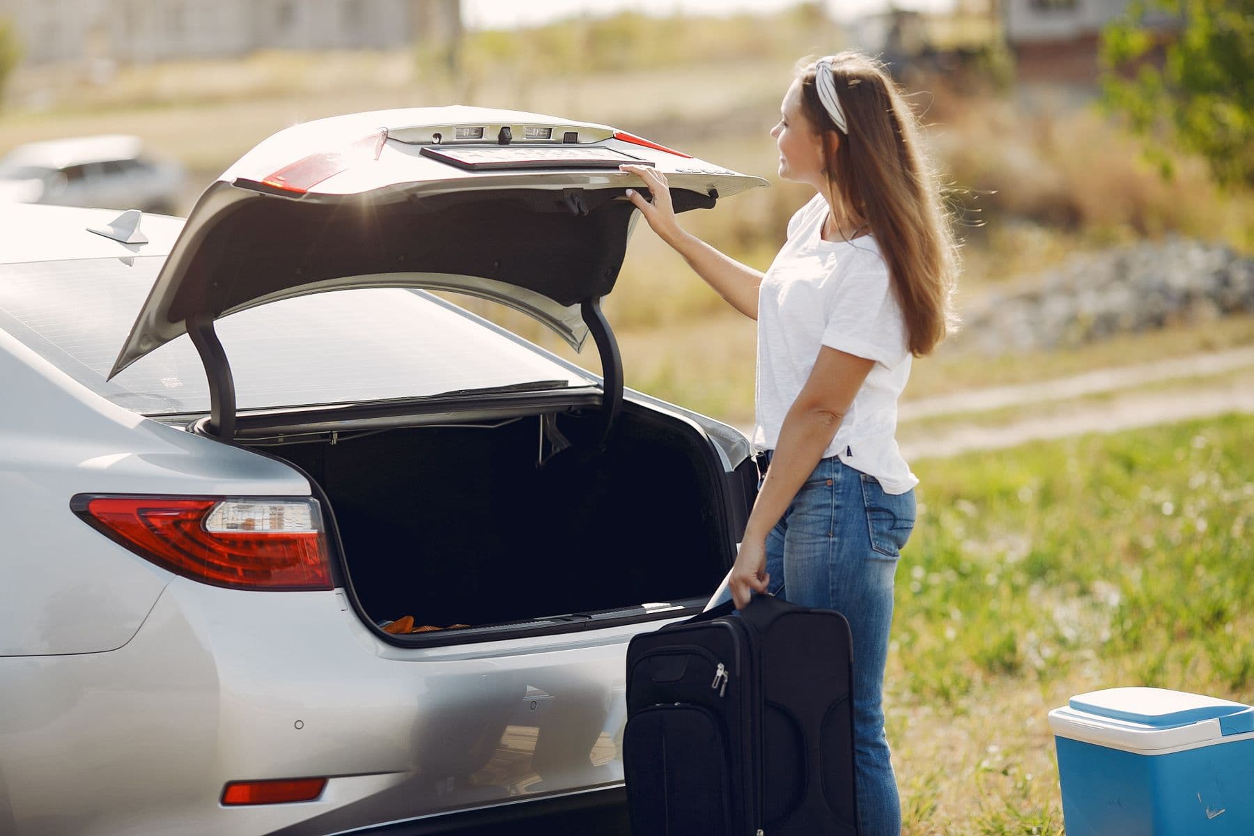 A cheerful traveller loading luggage into the open boot of a modern car
