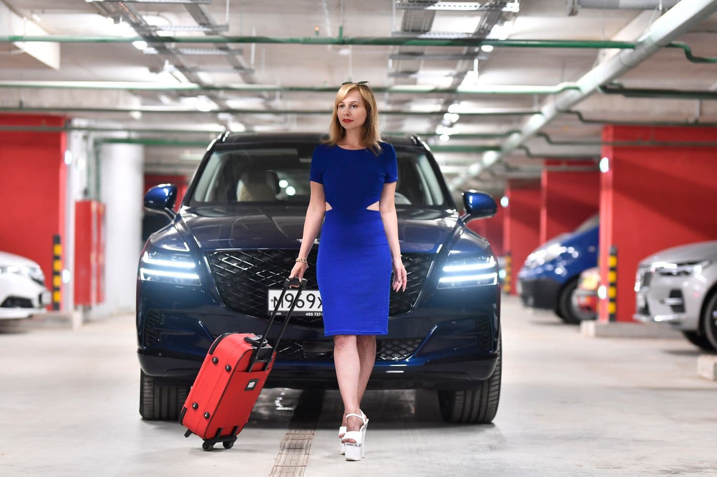 A traveller with a suitcase standing beside a luxury car in a parking garage
